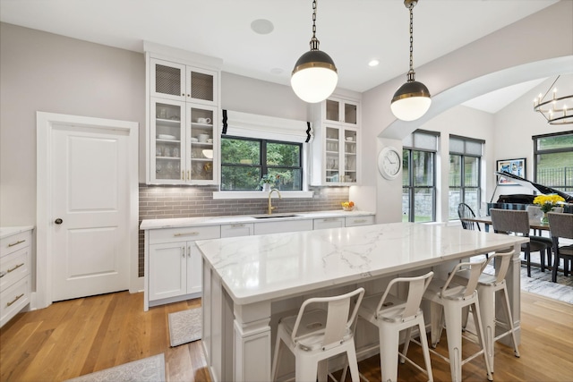 kitchen with sink, hanging light fixtures, a center island, white cabinets, and decorative backsplash