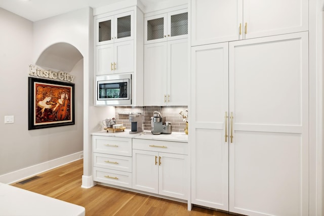 bar with stainless steel microwave, tasteful backsplash, light hardwood / wood-style floors, and white cabinets