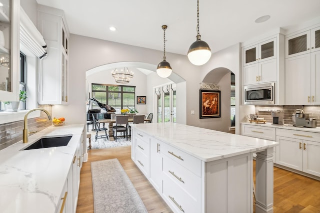 kitchen featuring sink, a center island, hanging light fixtures, stainless steel microwave, and white cabinets