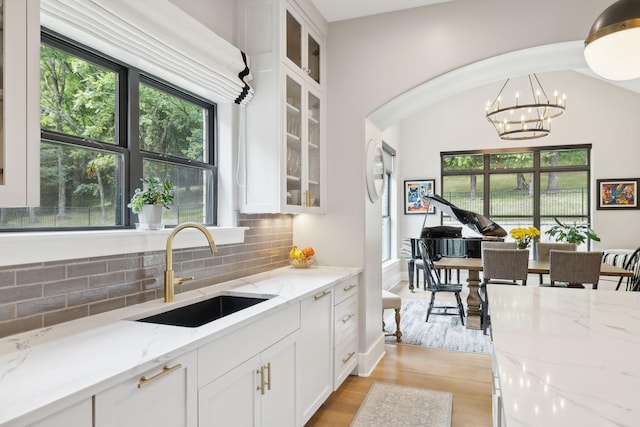 kitchen featuring sink, light stone counters, hanging light fixtures, white cabinets, and backsplash