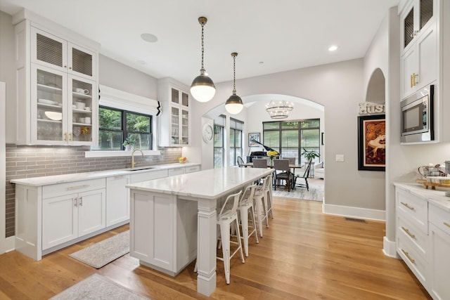 kitchen featuring pendant lighting, stainless steel microwave, white cabinetry, a center island, and light hardwood / wood-style flooring