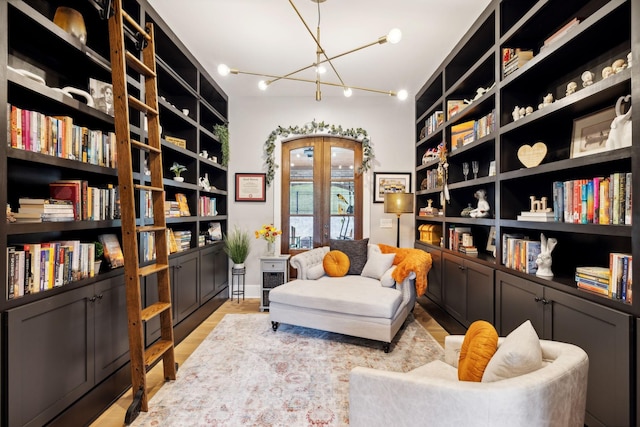 living area featuring a notable chandelier, built in features, light hardwood / wood-style floors, and french doors