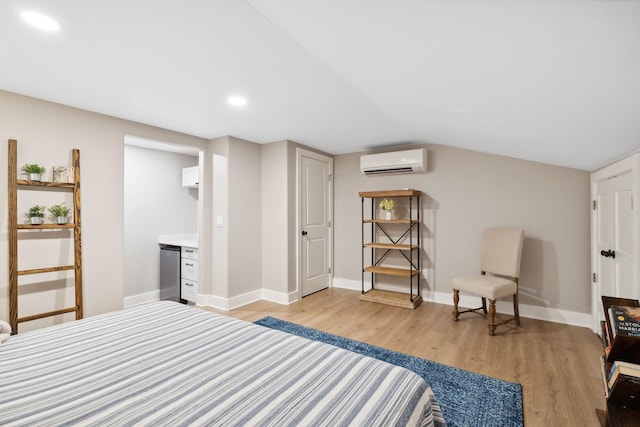 bedroom with an AC wall unit, lofted ceiling, light hardwood / wood-style floors, and ensuite bath