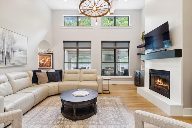 living room featuring a high ceiling, light wood-type flooring, an inviting chandelier, and a fireplace