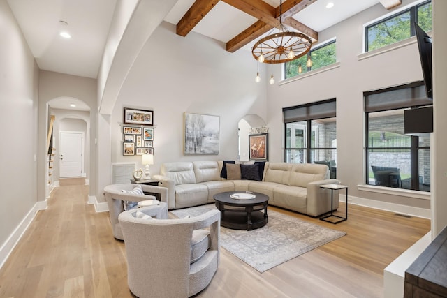 living room with beam ceiling, a towering ceiling, and light wood-type flooring