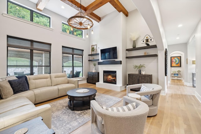 living room with beam ceiling, a towering ceiling, a wealth of natural light, and light hardwood / wood-style floors