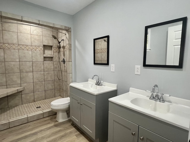 bathroom featuring a tile shower, vanity, wood-type flooring, and toilet