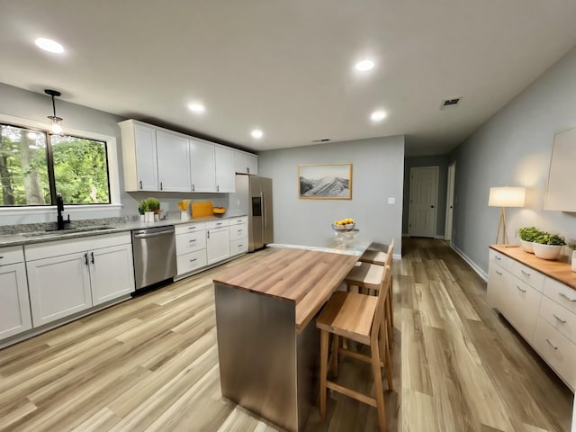 kitchen featuring butcher block countertops, white cabinetry, sink, hanging light fixtures, and stainless steel appliances