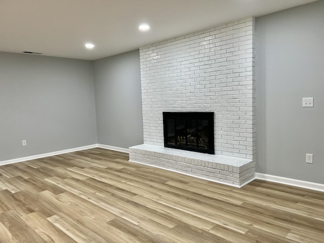 unfurnished living room featuring a brick fireplace and light hardwood / wood-style flooring