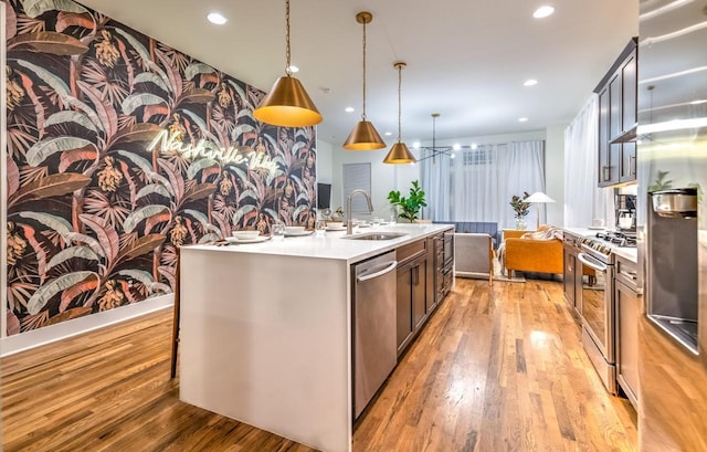 kitchen featuring sink, stainless steel appliances, light hardwood / wood-style floors, an island with sink, and decorative light fixtures