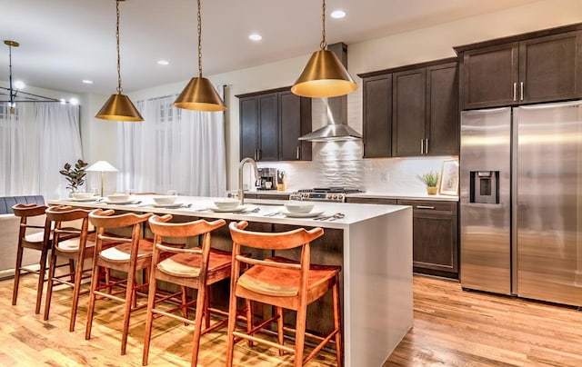 kitchen with appliances with stainless steel finishes, a kitchen breakfast bar, decorative light fixtures, and wall chimney range hood