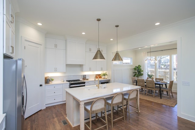 kitchen featuring decorative light fixtures, white cabinetry, stainless steel appliances, dark wood-type flooring, and a center island with sink