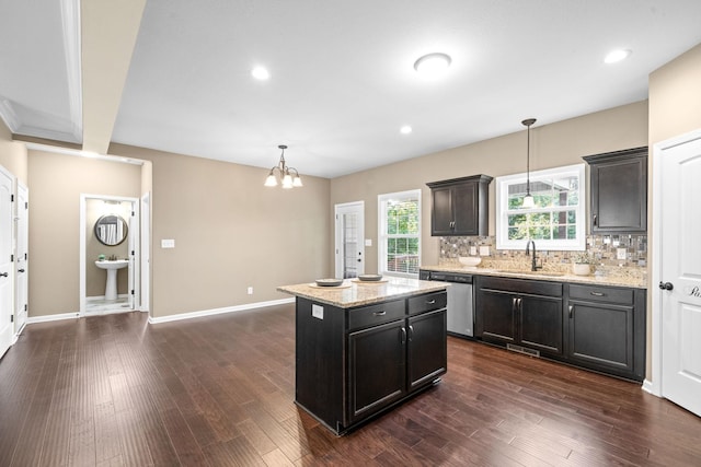 kitchen with sink, stainless steel dishwasher, a kitchen island, pendant lighting, and light stone countertops