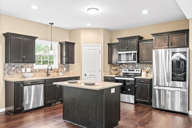 kitchen with sink, dark wood-type flooring, appliances with stainless steel finishes, a kitchen island, and decorative light fixtures