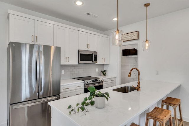 kitchen with sink, a breakfast bar area, white cabinets, hanging light fixtures, and stainless steel appliances