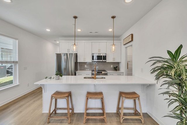 kitchen with appliances with stainless steel finishes, sink, white cabinets, a kitchen bar, and hanging light fixtures