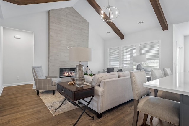 living room featuring a notable chandelier, dark hardwood / wood-style flooring, a tile fireplace, and vaulted ceiling with beams