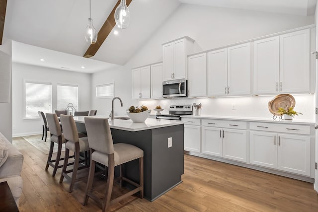 kitchen with pendant lighting, white cabinetry, a kitchen island with sink, stainless steel appliances, and tasteful backsplash