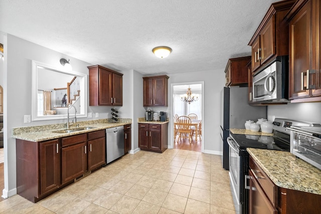 kitchen featuring light tile patterned flooring, appliances with stainless steel finishes, sink, light stone counters, and an inviting chandelier