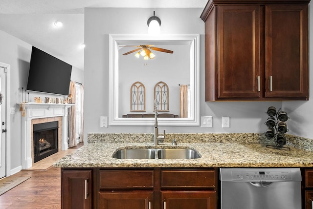 kitchen with sink, stainless steel dishwasher, a fireplace, and light stone counters