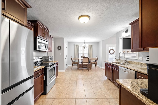 kitchen featuring appliances with stainless steel finishes, pendant lighting, sink, light tile patterned floors, and light stone counters