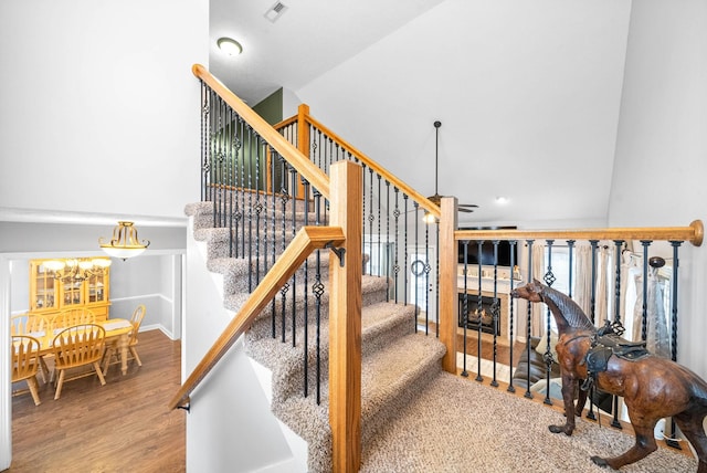 stairs with a tiled fireplace, wood-type flooring, and lofted ceiling