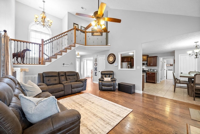 living room featuring light wood-type flooring, ceiling fan with notable chandelier, and high vaulted ceiling