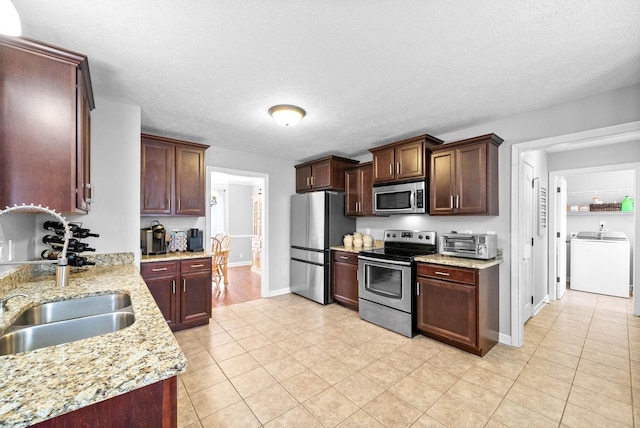 kitchen with light tile patterned flooring, sink, light stone counters, appliances with stainless steel finishes, and washer / clothes dryer