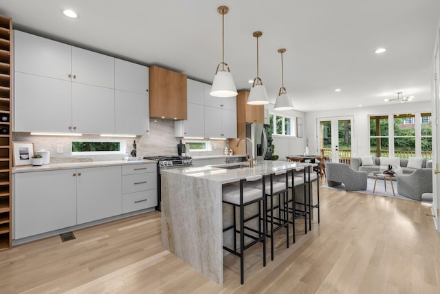 kitchen with white cabinetry, hanging light fixtures, a center island with sink, stainless steel appliances, and light hardwood / wood-style floors