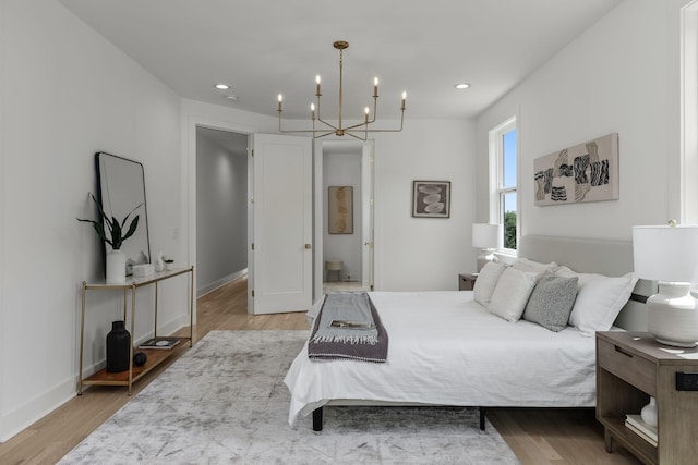 bedroom with ensuite bathroom, a notable chandelier, and light wood-type flooring