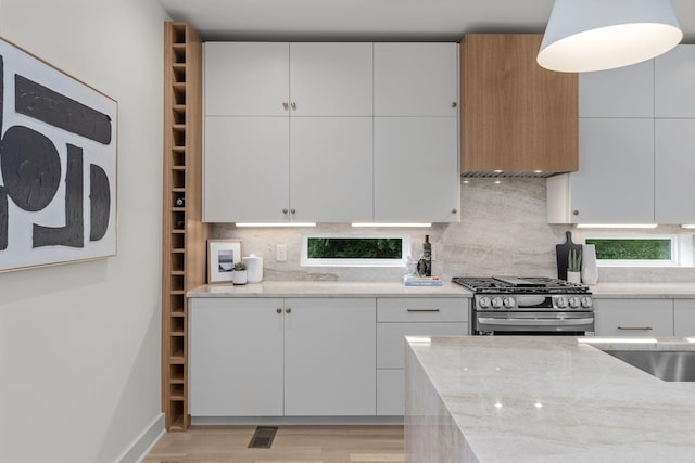 kitchen with backsplash, white cabinets, light stone countertops, and stainless steel gas stove