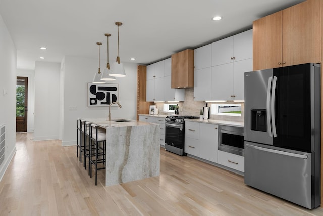 kitchen featuring an island with sink, white cabinets, decorative backsplash, hanging light fixtures, and stainless steel appliances