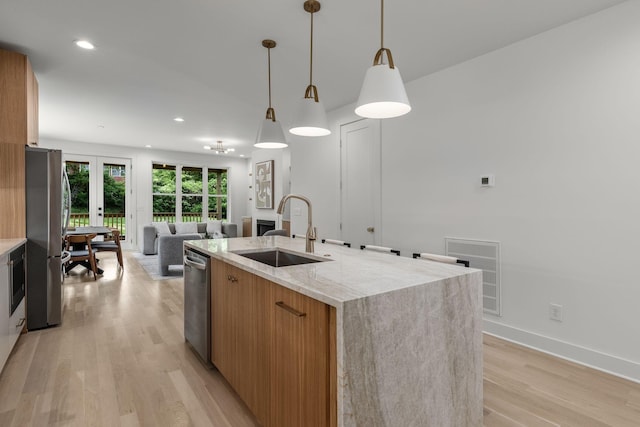 kitchen with decorative light fixtures, sink, stainless steel appliances, a center island with sink, and light wood-type flooring