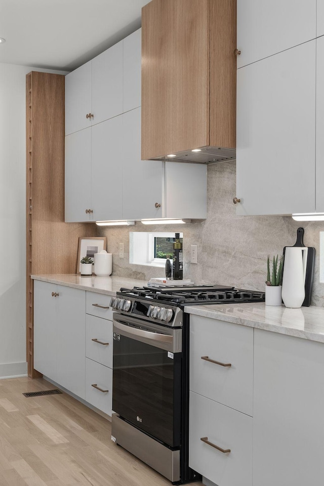 kitchen with light hardwood / wood-style flooring, white cabinetry, stainless steel range with gas stovetop, tasteful backsplash, and light stone countertops