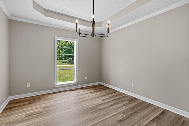 spare room with a chandelier, a raised ceiling, a textured ceiling, and light wood-type flooring