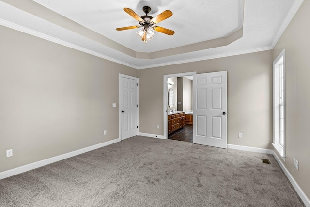 unfurnished bedroom featuring dark colored carpet, connected bathroom, ceiling fan, and a tray ceiling