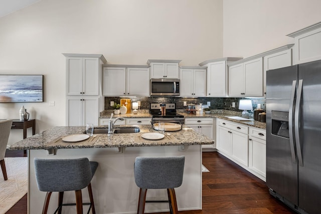 kitchen with sink, a center island with sink, stone counters, stainless steel appliances, and a high ceiling