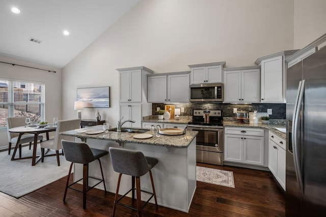 kitchen featuring backsplash, high vaulted ceiling, dark hardwood / wood-style floors, stainless steel appliances, and an island with sink