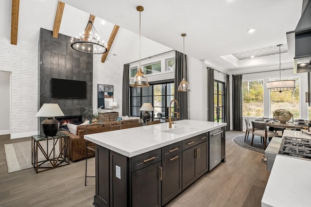 kitchen featuring hardwood / wood-style floors, a fireplace, decorative light fixtures, an island with sink, and sink