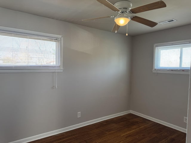 empty room with plenty of natural light, dark wood-type flooring, and ceiling fan