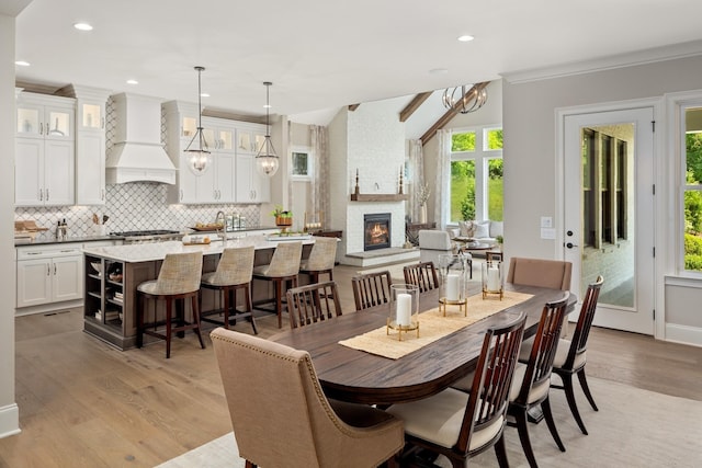 dining space with a notable chandelier, ornamental molding, a fireplace, and light hardwood / wood-style floors