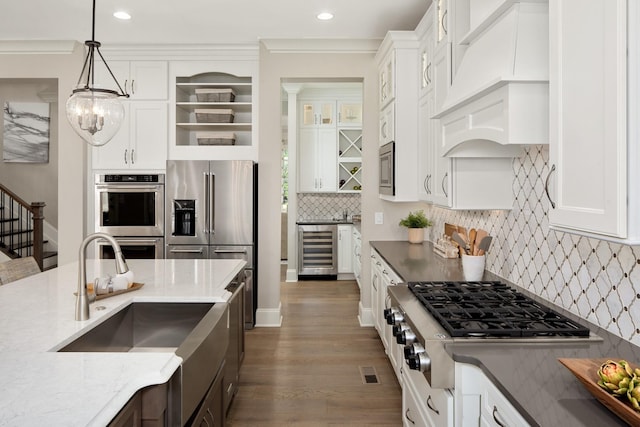 kitchen with pendant lighting, appliances with stainless steel finishes, white cabinetry, premium range hood, and beverage cooler