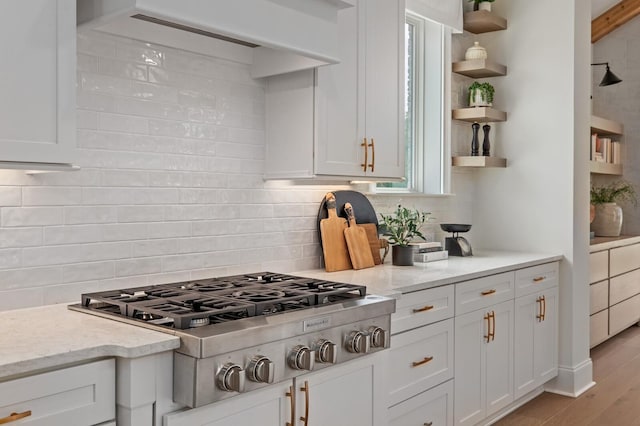 kitchen with tasteful backsplash, stainless steel gas cooktop, white cabinets, and light stone counters