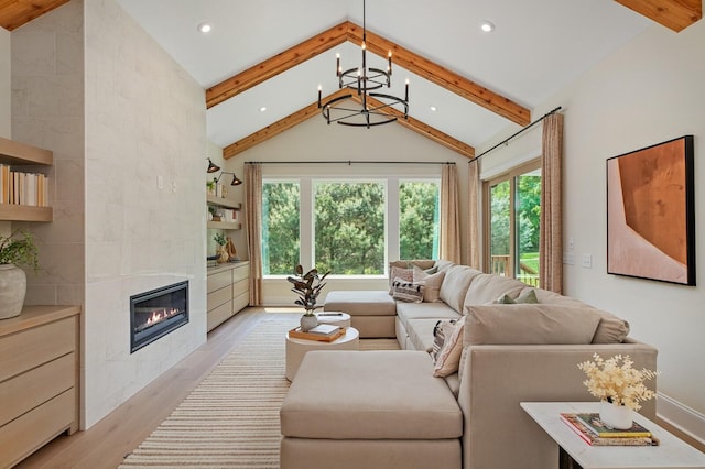 living room with lofted ceiling with beams, a tiled fireplace, light hardwood / wood-style floors, and a notable chandelier