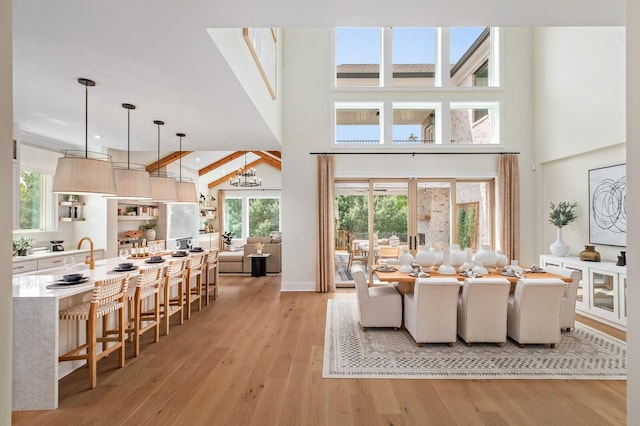 living room featuring french doors, a chandelier, beamed ceiling, a towering ceiling, and light hardwood / wood-style floors