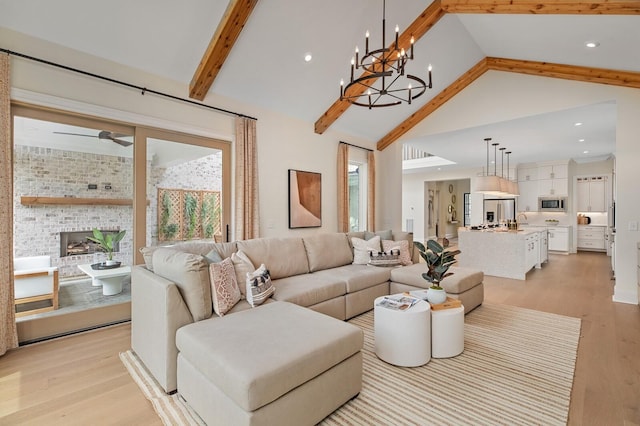 living room featuring sink, a brick fireplace, light hardwood / wood-style flooring, a notable chandelier, and beam ceiling