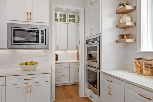 kitchen with light stone counters, light hardwood / wood-style flooring, appliances with stainless steel finishes, decorative backsplash, and white cabinets