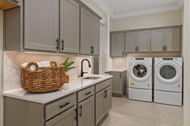 clothes washing area featuring cabinets, ornamental molding, sink, and washing machine and dryer