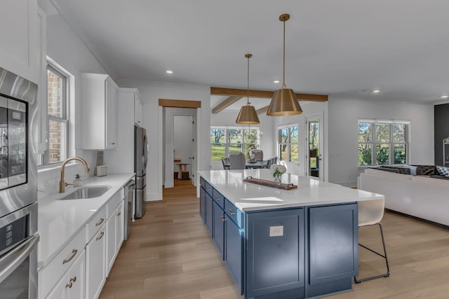 kitchen with appliances with stainless steel finishes, sink, white cabinets, hanging light fixtures, and blue cabinetry