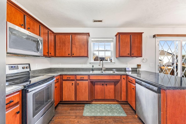 kitchen with sink, kitchen peninsula, stainless steel appliances, dark wood-type flooring, and a textured ceiling